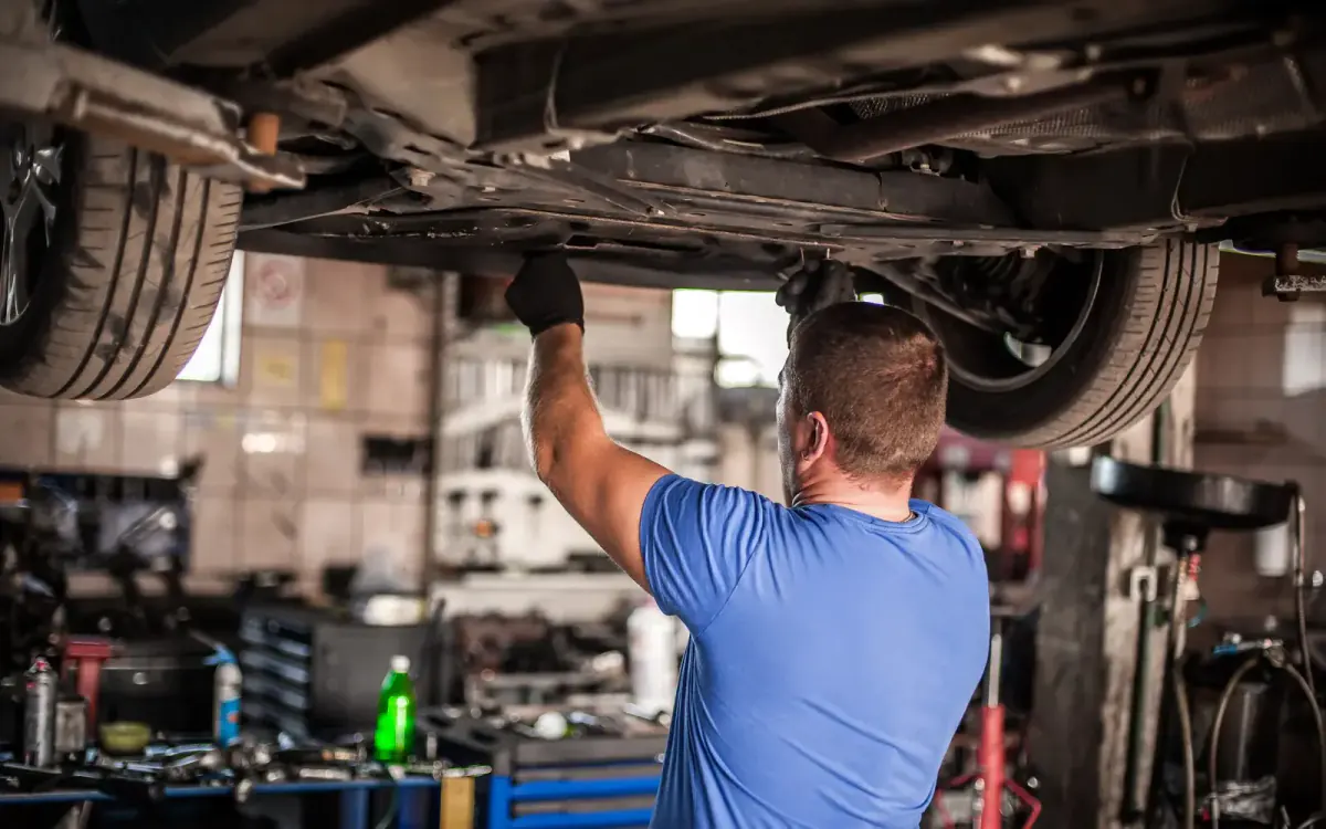 Mechanic inspecting the underside of a car on a lift — repair or sell a car with a blown engine